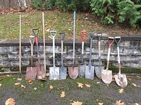 Full lineup of 11 garden tools against stone wall