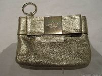 Front of metallic gold Kate Spade coin purse showing bow and logo plaque