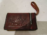 Front view of brown leather wallet with embossed wildlife scene, wrist strap and visible zipper