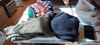 Three folded sweaters on table: patterned, olive, black