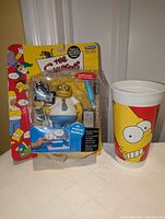 Front view of sealed Dr. Marvin Monroe figure beside Bart Simpson KFC cup