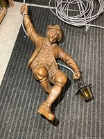 Full view of carved wood figure with cord and lantern