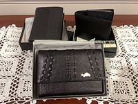 Three boxed black leather wallets on lace mat