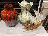 Group shot of red/black swirl vase, white ornate vase, wooden sailboat