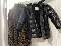 Front view of both coats hanging, showing black puffer and leopard faux-fur