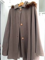 Full view of brown wool cape hanging, showing collar fur trim and front buttons