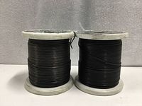 Front view of two full spools of black tie wire on white plastic bases