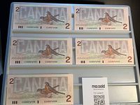 Backs of five Canadian $2 bills showing American robin and sequential serial numbers