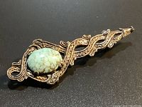 Front view of ornate metal brooch with turquoise stone