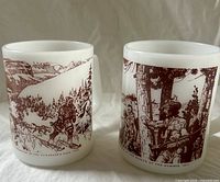 Both white milk glass explorer mugs, side graphics visible