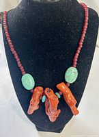 Front view of full necklace on stand showing coral branches, turquoise ovals, red bead strand