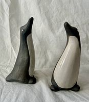 Front view of both ceramic penguins, showing grey-black bodies and white crackle-glazed breasts