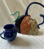 Blue jug and multi-color teapot-form vase side by side