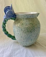 Full view of pitcher showing braided handle and blue flower