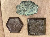 Three ceramic plates on sofa: irregular greenish-blue, hexagonal dark brown, square dark brown