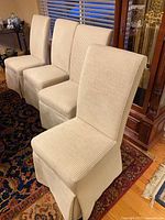 Front view of three slipcovered parsons chairs showing striped fabric and skirted bases
