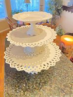 Three white ceramic cake stands stacked, showing lattice rims and pedestals