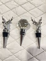 Three wine stoppers laid out: two deer head chrome, one faceted glass knob