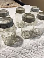 Six clear glass canning jars with lids on quilt background