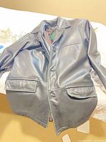 Full view of black leather coat laid flat showing front, buttons, pockets