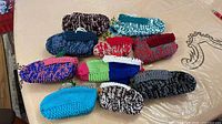 Group shot of twelve pairs of handmade knit slippers in assorted colours