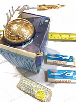 Overall lot showing Vostok souvenir globe, box, and three sugar packets with measuring tape for scale