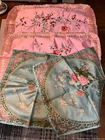 Four pillow covers laid out: two pink ruffled shams and two turquoise square covers