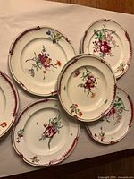 Group view of several plates displaying floral centers and burgundy rims