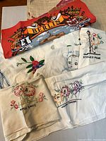 Group of folded linens showing Berlin print and multiple embroidered towels