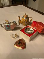 Group shot of all five items: two cloisonné teapots, sake cup in box, crystal pig figurine, enamel brooch