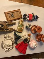 Group shot showing all items: sand painting, pueblo sculpture, fish plaque, cat figurine, dolls, redware candle holders, Navajo vase, miniature pitcher