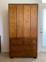 Closed armoire front showing oak grain, bi-fold upper doors, five drawers, brass campaign pulls