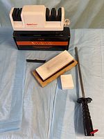 Group shot showing all sharpeners: electric unit, handheld pull-through, whetstone on base, dressing stone, honing rod