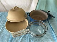 Group shot showing glass double boiler, stoneware clay cooker opened, and blue enamel Dutch oven with lid