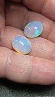 Pair of oval cabochon opals in hand showing size and play-of-color