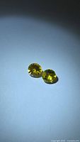 Pair of yellow-green round sphene gemstones on neutral background