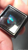 Front view of pear cabochon black opal showing blue and green play-of-color in display box