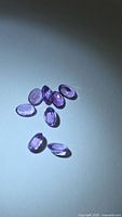 Group of eight oval cut purple amethysts under spotlight