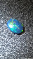 Oval black opal cabochon showing play-of-colour on textured background
