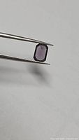 Octagon-cut purple spinel held by tweezers, face view