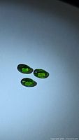 Three green oval chrome diopside gemstones on white background