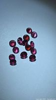 Group of 13 round deep pink rhodolite garnets on white background