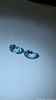 Pair of oval blue topaz gemstones on light background
