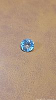 Top view of round blue aquamarine gemstone on tan surface
