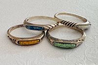 Four sterling silver rings with coloured inlays on flat surface