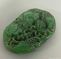 Front view of green jade pendant showing koi fish and floral carving