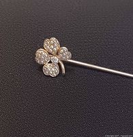 Stick pin close-up showing four-leaf clover head with seed pearls and diamond