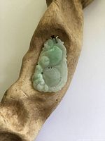 Front view of carved jade pendant on driftwood display