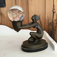 Side view of bronze figure kneeling and presenting glass orb