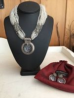 Full view of necklace on display bust, earrings and pouch beside